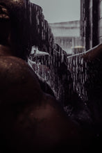 Load image into Gallery viewer, Black man with a beard in a modern contemporary home enjoying his beautifully designed candles by HAUME that are sitting on the ledge of a matte black tiled shower as the warm water runs over his beard, body, and muscles.
